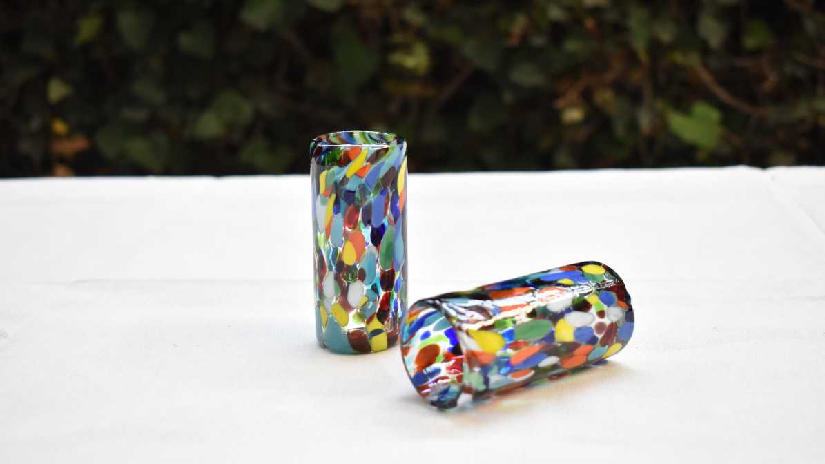 dos tequileros de vidrio soplado decorado confetti multicolor sobre una mesa con mantel blanco